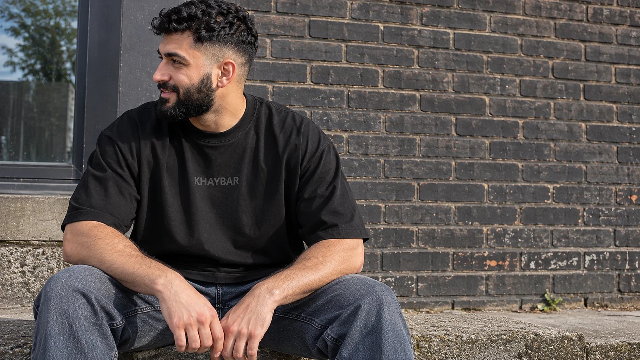Khaybar chest print tee, seated on brick steps
